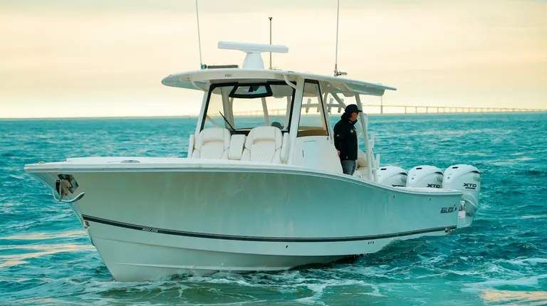 White center-console boat with triple XTO outboard engines running on choppy turquoise water at sunset, with a person standing at the helm.
