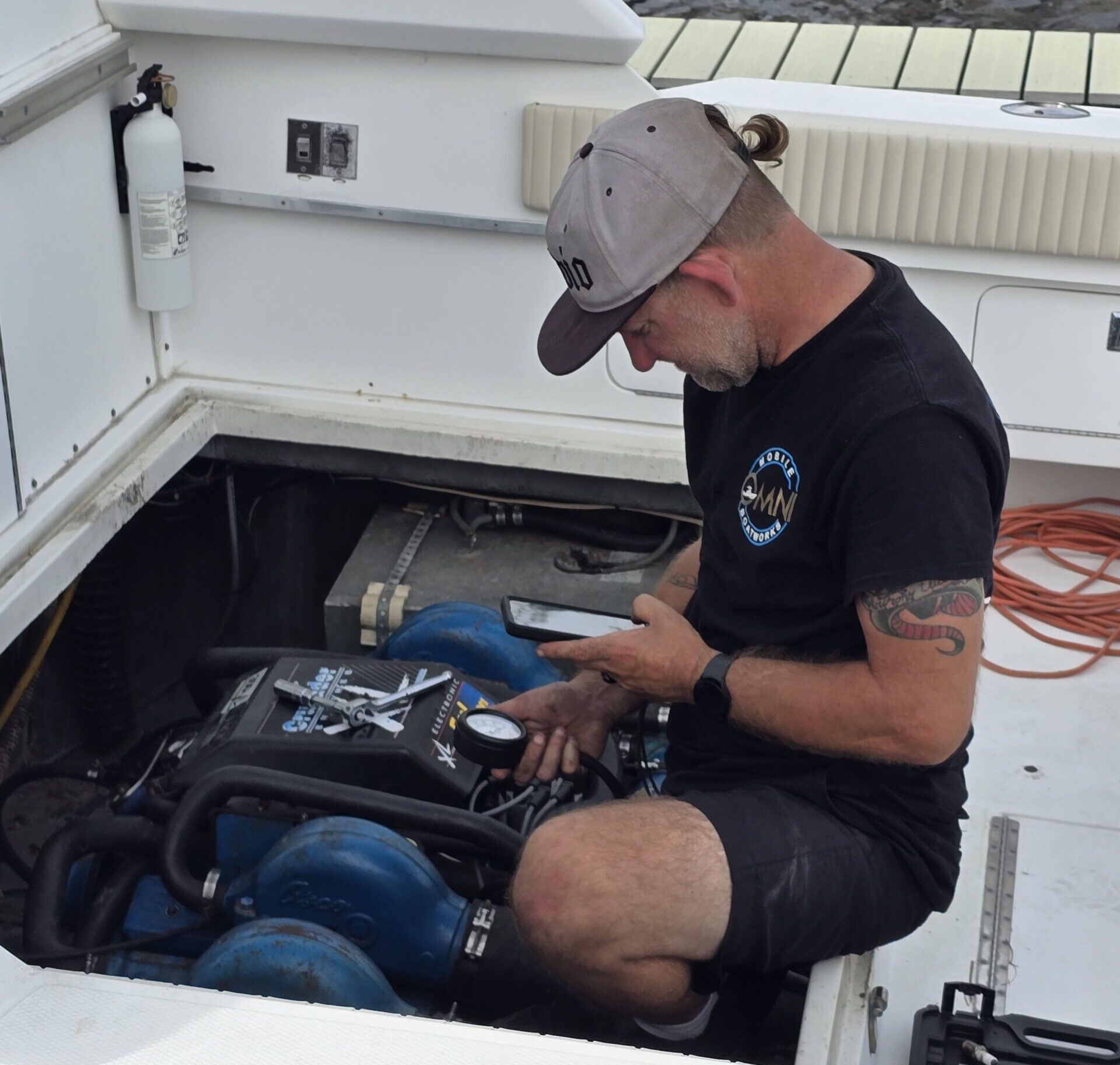 Technician checking a boat engine with a pressure gauge and tablet at Omni Mobile Boatworks.