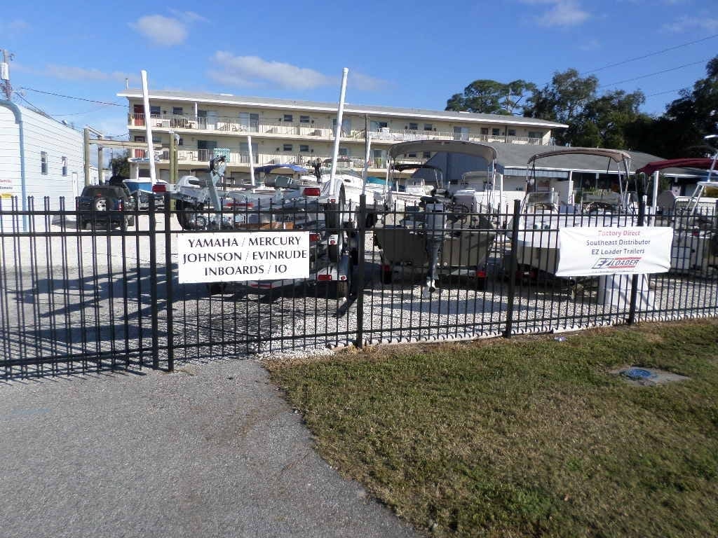 Boat sales yard with Yamaha, Mercury, Johnson and Evinrude engine signage and boats on EZ Loader trailers behind a black metal fence, town unknown.