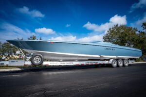 Light blue Donzi performance boat on a multi-axle trailer on a paved lot under a blue sky.