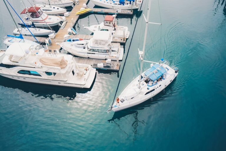 Aerial view of white motor yachts and a sailboat moored along a wooden dock in a marina.