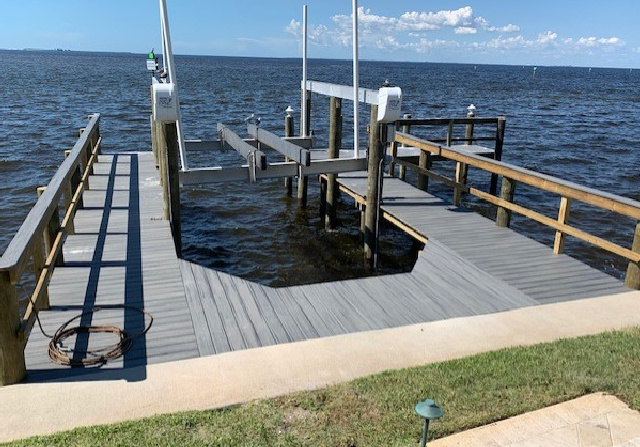 Gray composite boat dock with a boat lift and wooden railings extending over calm bay water.