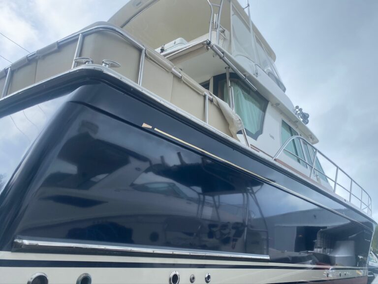 Black-hulled motor yacht with cream canvas enclosures and stainless steel railings, photographed from the stern at a dock.