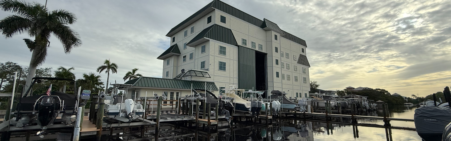 Multi-story dry-stack boat storage building with boats on racks and docked boats along a canal waterfront.