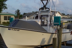 White fishing boat with a dark canvas helm cover and Florida registration tied up at a residential dock with a house in the background.