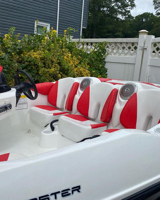 Red and white bowrider boat seating and helm console on a boat labeled Monster, parked beside a white vinyl fence and shrubs.