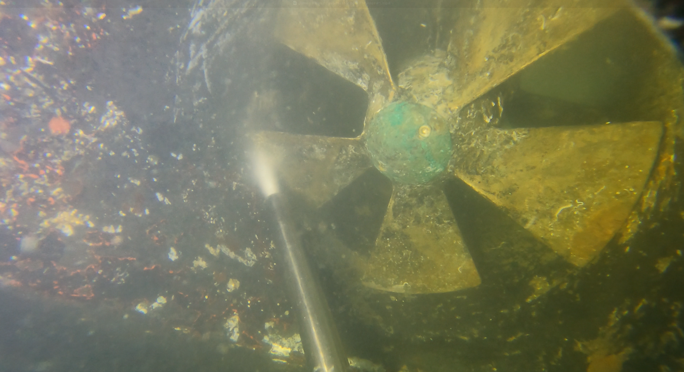 Underwater photograph of a five-blade bronze propeller being cleaned with a water-jet wand, marine growth visible on the blades.