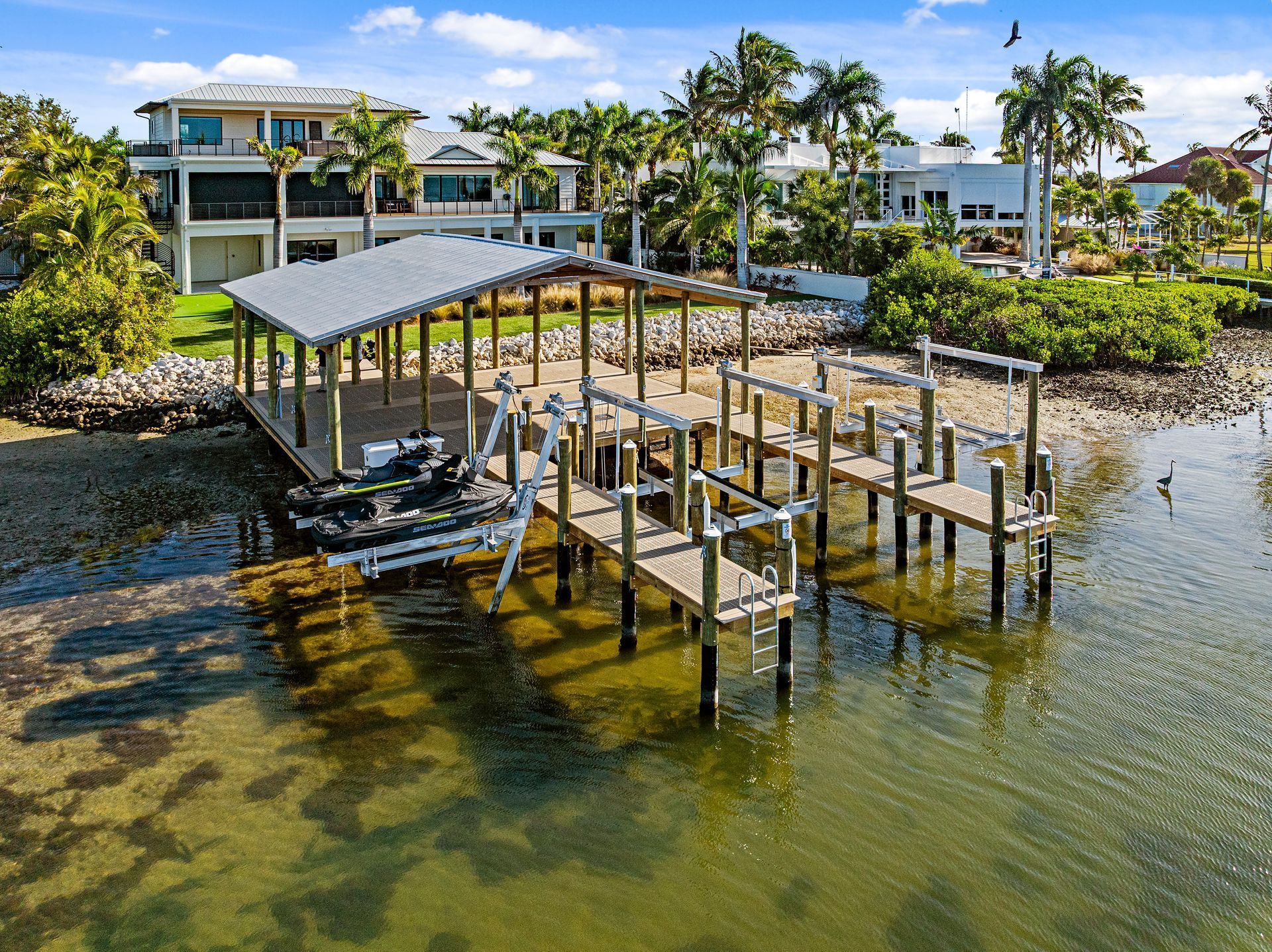Covered dock with aluminum personal watercraft lifts holding two Sea-Doo jet skis, with a waterfront home behind it.