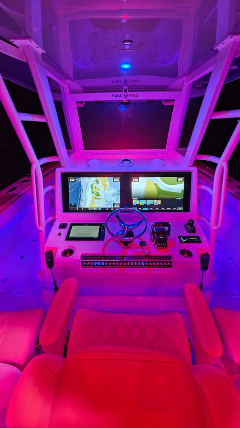 Helm station with dual chartplotter displays, a ship's wheel, and throttle controls inside a center console boat, lit with purple and red LED accents.