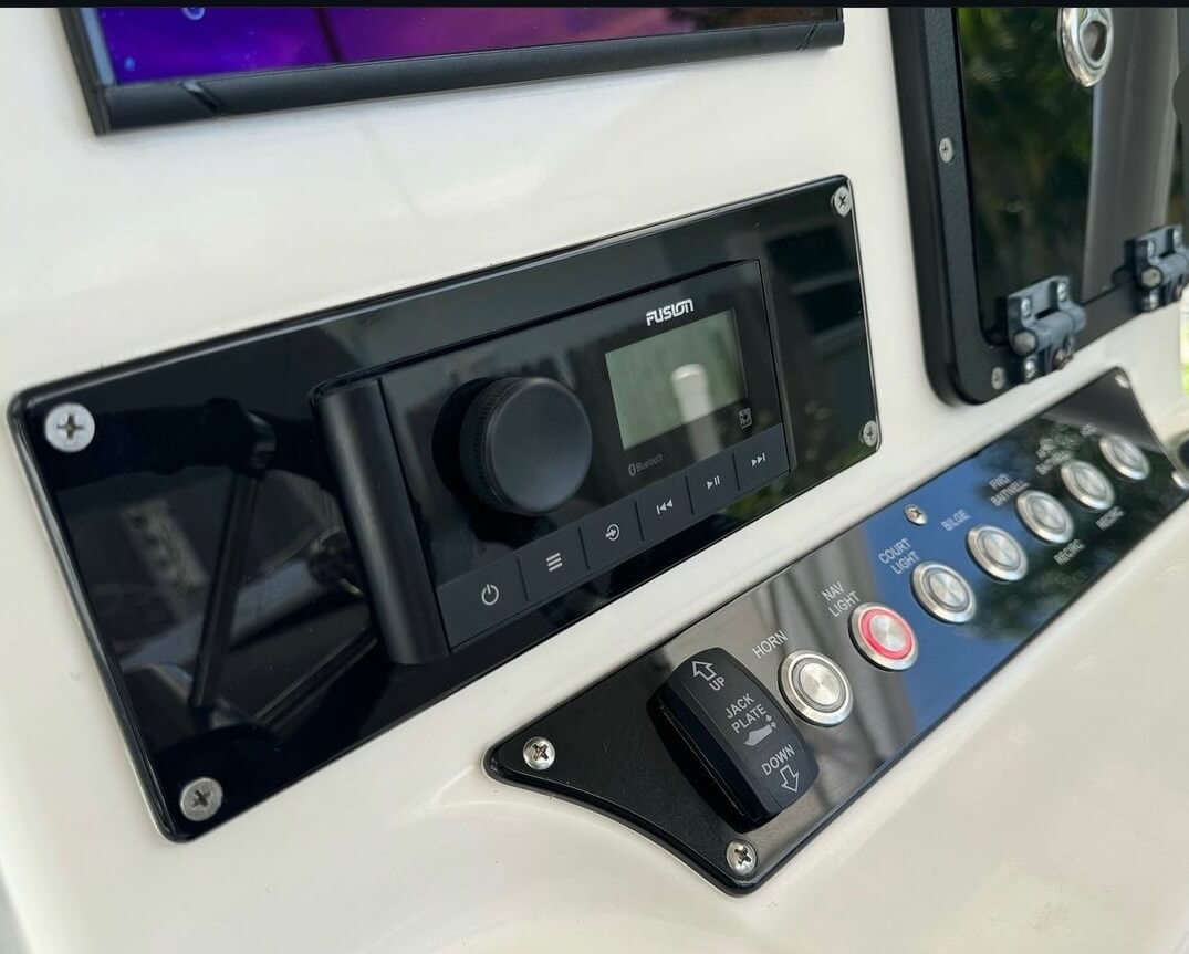 Fusion marine stereo head unit with Bluetooth and a switch panel for jack plate, horn, nav light, courtesy light, bilge, and livewell controls mounted on a boat console.