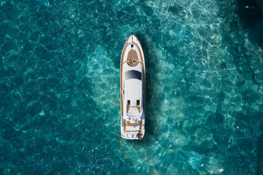 Aerial view of a white motor yacht with teak trim anchored in clear turquoise water.