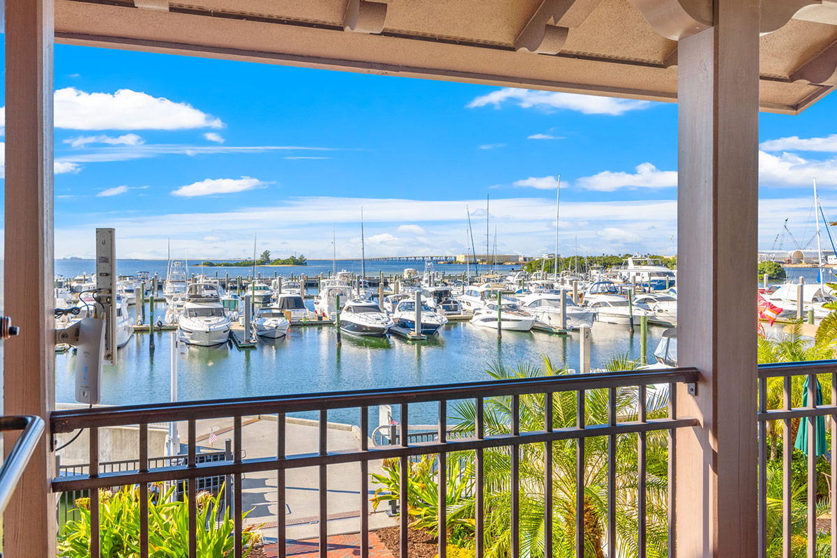 Rows of docked motor yachts and sailboats at a marina, viewed from a covered balcony overlooking the water.