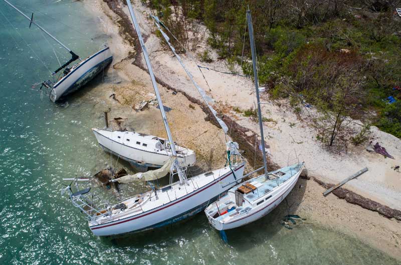 Aerial view of several grounded sailboats stranded on a sandy shoreline with turquoise water beside them.
