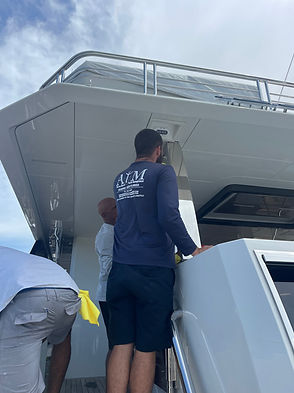 Crew member boarding a white motor yacht, wearing a navy shirt with the ANM logo.