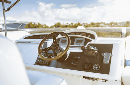 Boat helm station with a wood-rimmed steering wheel and instrument panel overlooking the water.