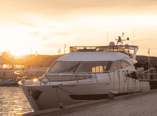 Luxury motor yacht MY KARAT moored at a wooden dock during sunset, with harbor lights in the background.